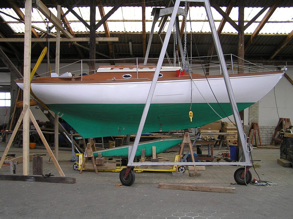 Klassische Segelyacht mit grünem Unterwasserschiff am Portalkran in der Halle
