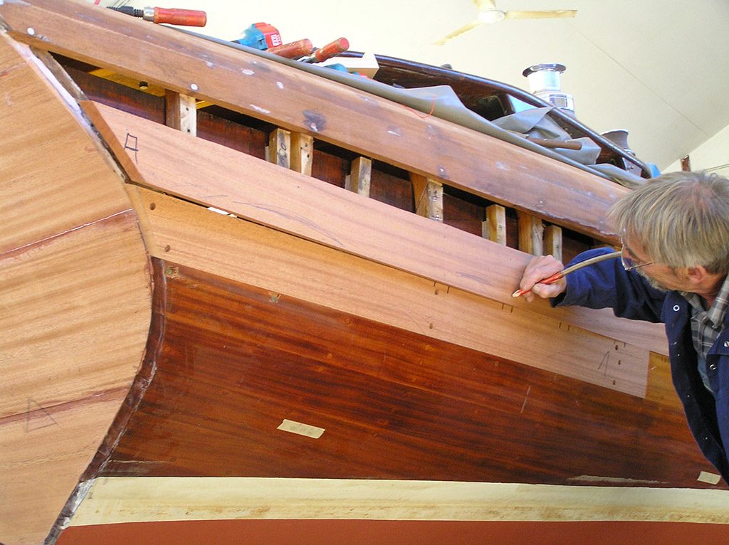 Bootsbauer zeichnet neue Planken an einem Holzrumpf an